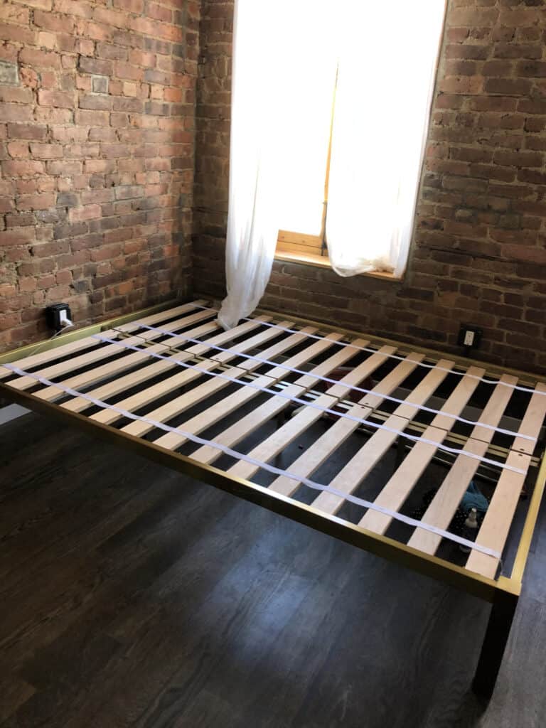 Bed frame with wooden slats and a brick wall.